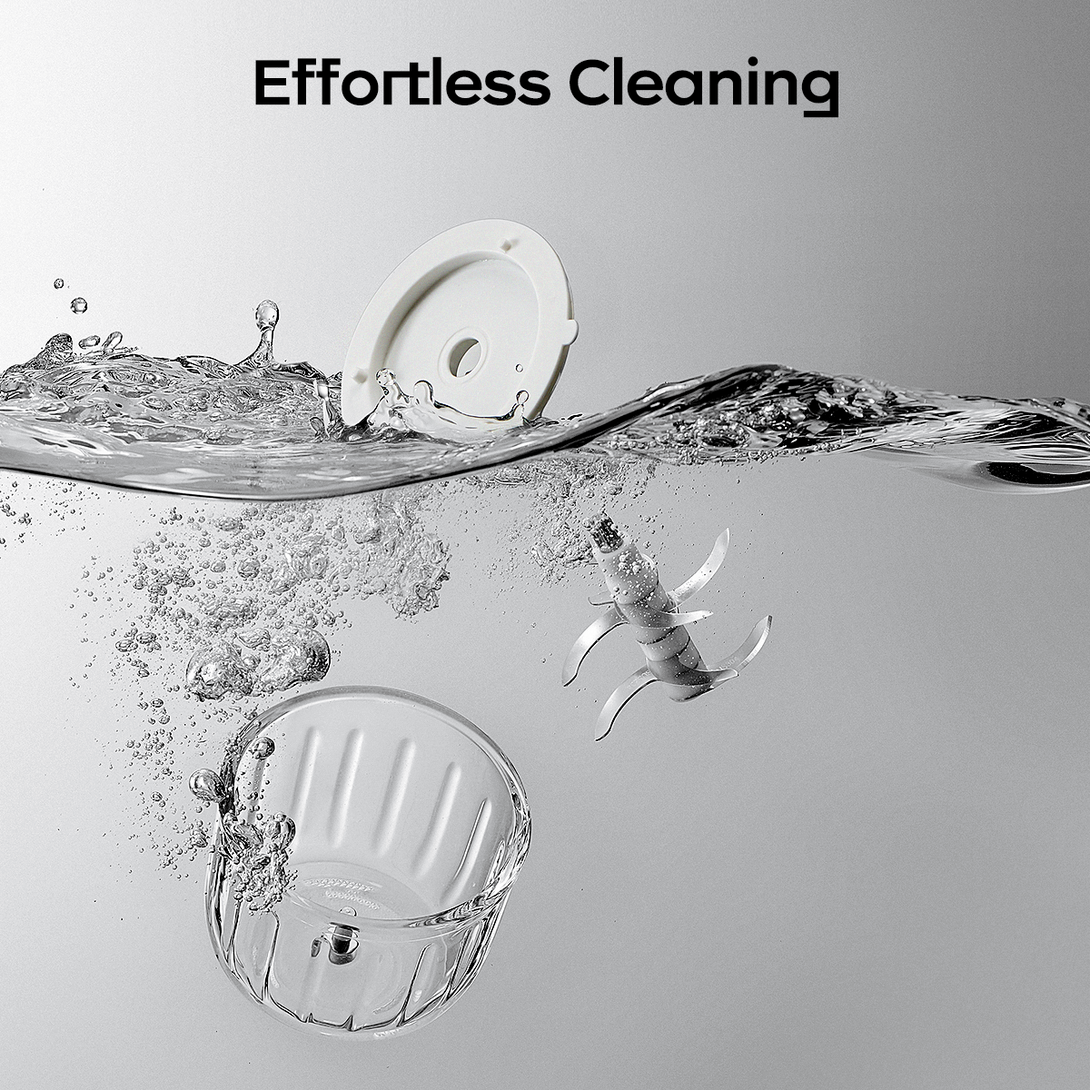 This image displays parts of a food processor amidst splashing water, illustrating “Effortless Cleaning”. Components such as a white cover, a transparent glass bowl, and stainless - steel blades are submerged, highlighting the ease of maintaining the product.
