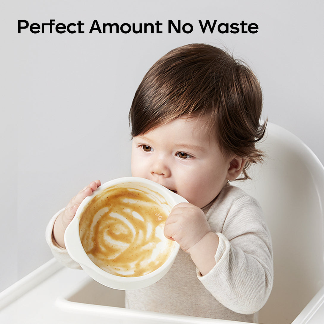 This image depicts a baby seated in a high - chair, holding a bowl with both hands and eating. The bowl contains a swirled food mixture. At the top, the text “Perfect Amount No Waste” is shown
