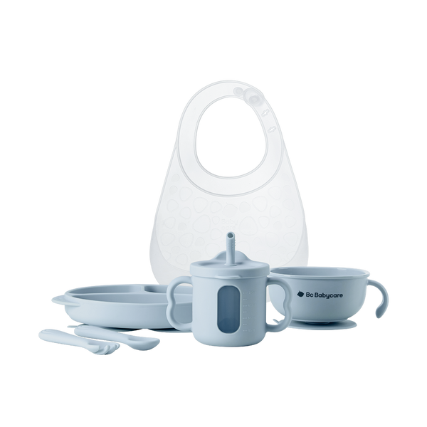 White background image of a blue baby tableware set, including a bib, plate, fork and spoon, cup, and bowl.