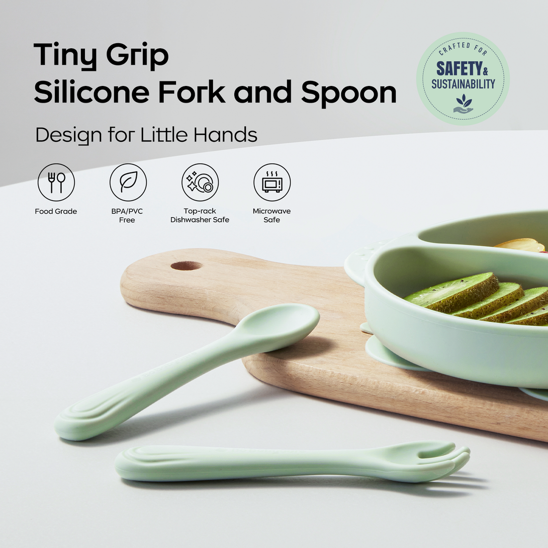 A green silicone fork and spoon set and a plate on a table, with food-grade and safety labels at the top-left and a sustainability logo at the top-right.