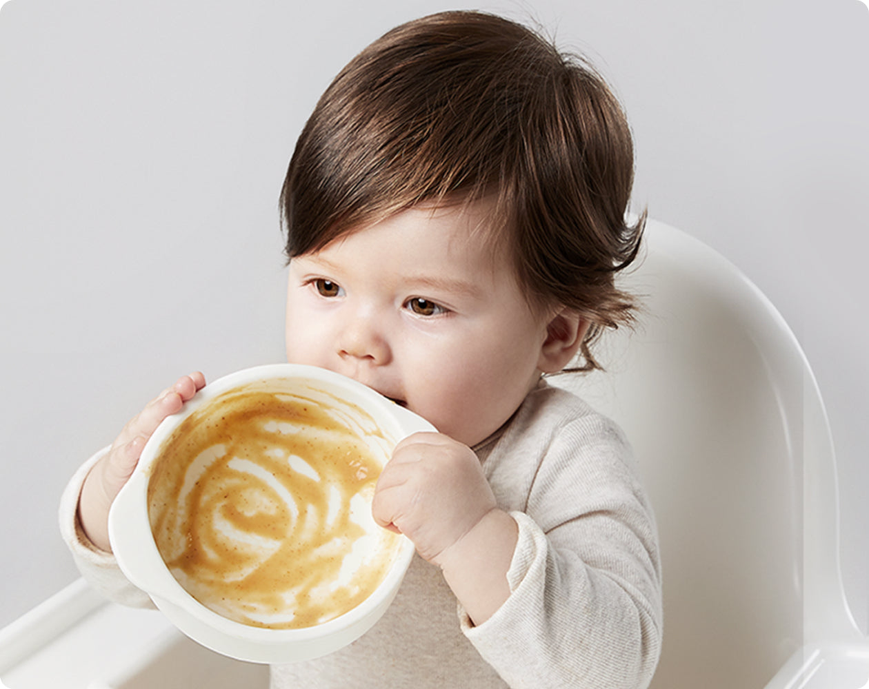 Baby with feeding bowl representing the borosilicate glass and food-contact materials used in the Baby Food Maker.
