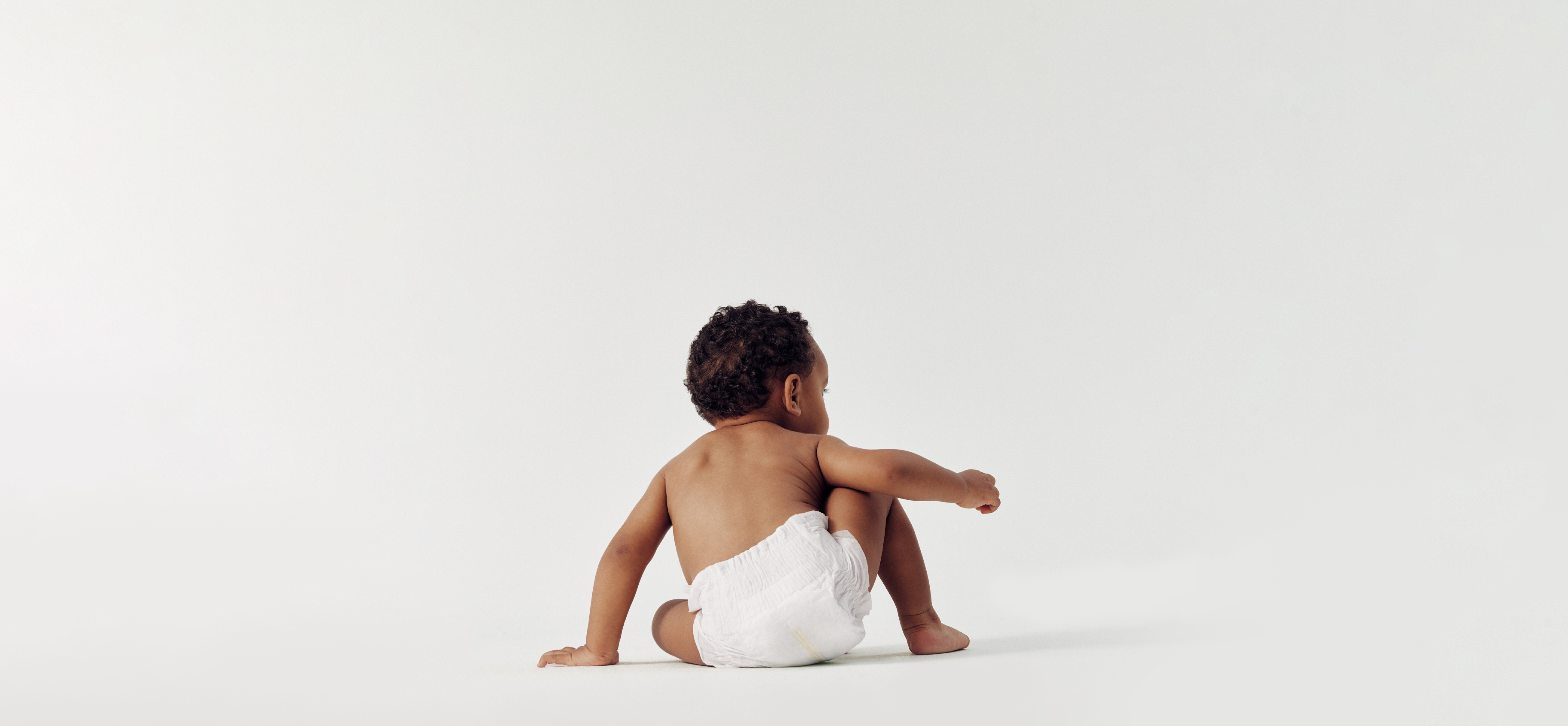 A back view of a baby wearing a Cloud Skin diaper, sitting on a white background. The image highlights the slim fit and soft, cloth-like texture of the premium infant diaper.